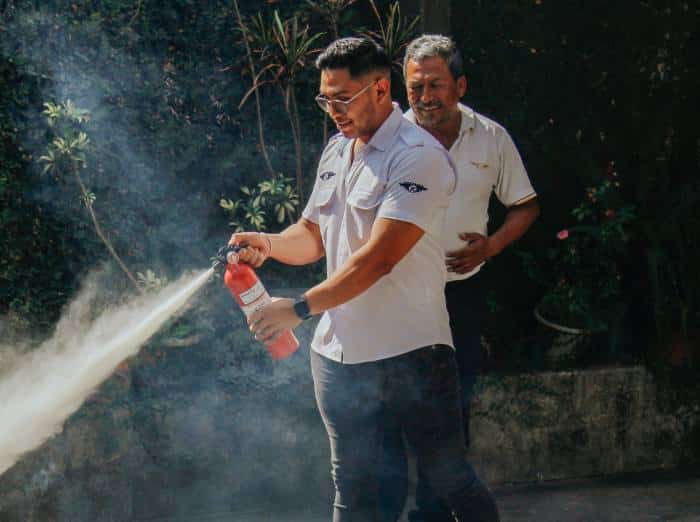 two men in work shirts learning how to use a fire extinguisher