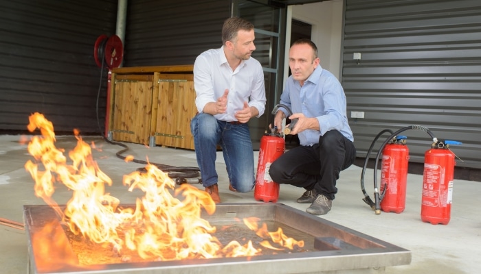 two men are crouched down discussing a controlled fire in a training environment